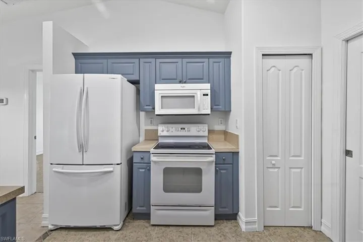 Kitchen featuring blue cabinetry, white appliances, light tile patterned floors, light countertops, and high vaulted ceiling