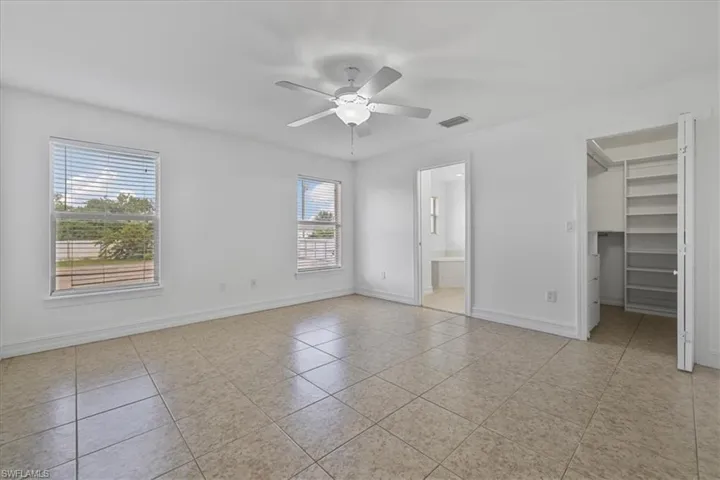 Unfurnished bedroom with a walk in closet, light tile patterned floors, ensuite bathroom, and a ceiling fan