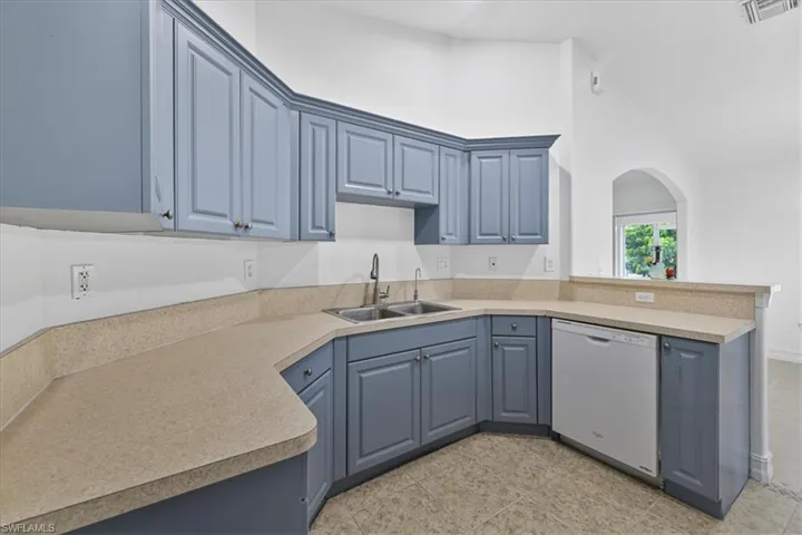 Kitchen with blue cabinets, white dishwasher, a peninsula, high vaulted ceiling, and light countertops