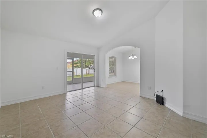 Empty room featuring a chandelier, vaulted ceiling, light tile patterned flooring, and arched walkways