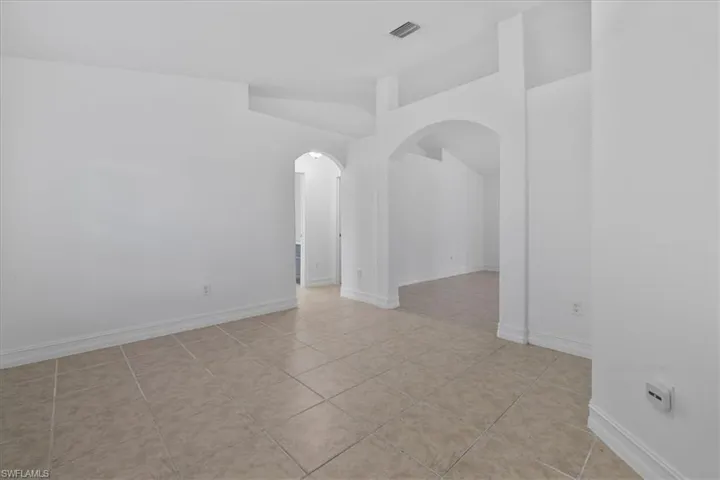 Empty room featuring arched walkways, lofted ceiling, and light tile patterned floors
