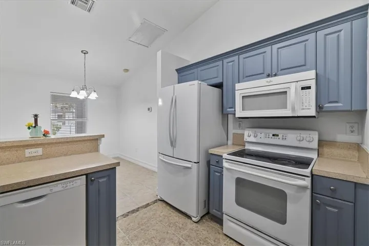 Kitchen with vaulted ceiling, white appliances, blue cabinets, pendant lighting, and light tile patterned flooring
