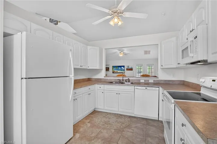 Kitchen with white appliances, white cabinetry, light tile patterned floors, vaulted ceiling, and a ceiling fan