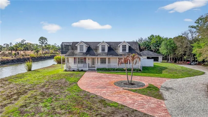 Cape cod-style house with covered porch, a front yard, curved driveway, and a water view