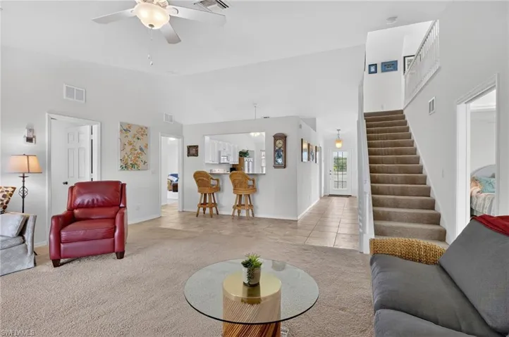 Living area featuring light carpet, light tile patterned flooring, vaulted ceiling, and a ceiling fan