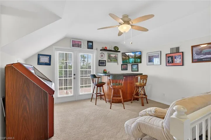 Indoor dry bar with a ceiling fan, dark countertops, light carpet, and lofted ceiling