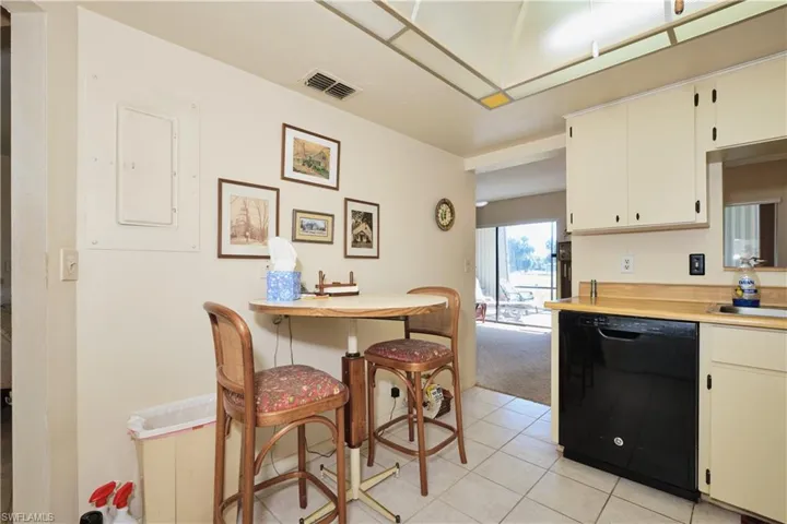 Kitchen with light countertops, black dishwasher, light tile patterned flooring, electric panel, and light colored carpet