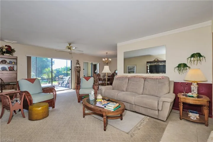 Carpeted living area featuring a ceiling fan, a chandelier, and ornamental molding
