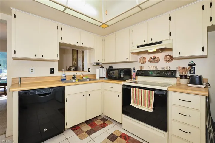 Kitchen featuring black appliances, light countertops, under cabinet range hood, and cream cabinetry