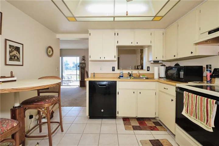 Kitchen with black appliances, light countertops, light tile patterned floors, under cabinet range hood, and light colored carpet