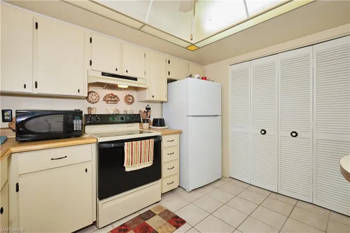 Kitchen with cream cabinets, white appliances, light countertops, light tile patterned floors, and under cabinet range hood