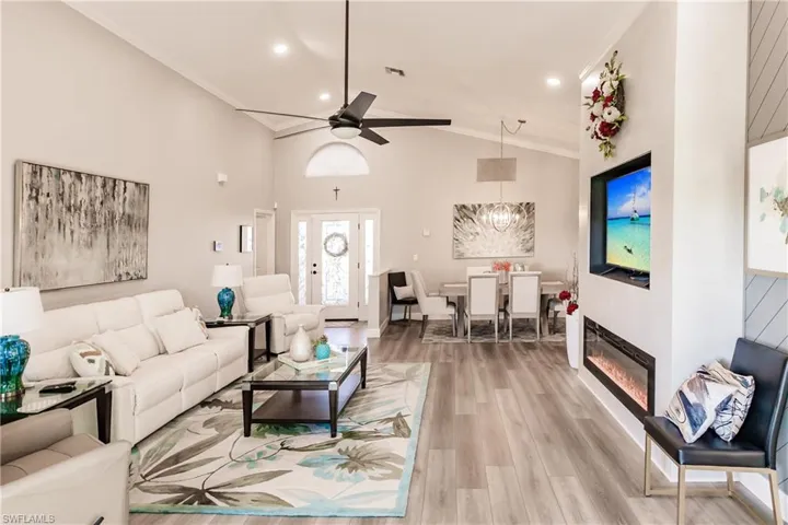 Living room with hardwood / wood-style flooring, ceiling fan with notable chandelier, ornamental molding, and high vaulted ceiling