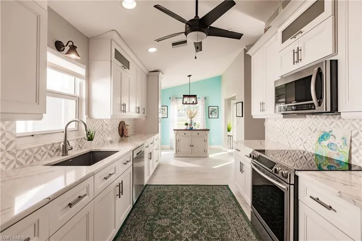 Kitchen with sink, hanging light fixtures, stainless steel appliances, lofted ceiling, and white cabinets
