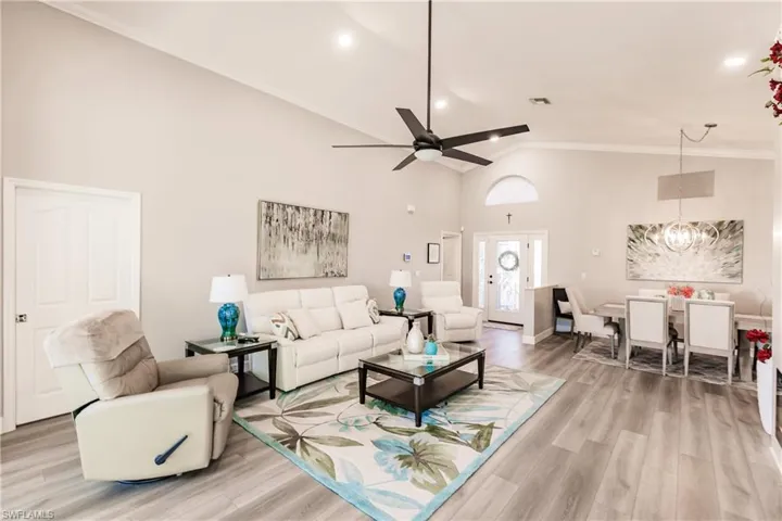 Living room with high vaulted ceiling, light hardwood / wood-style floors, ceiling fan with notable chandelier, and ornamental molding