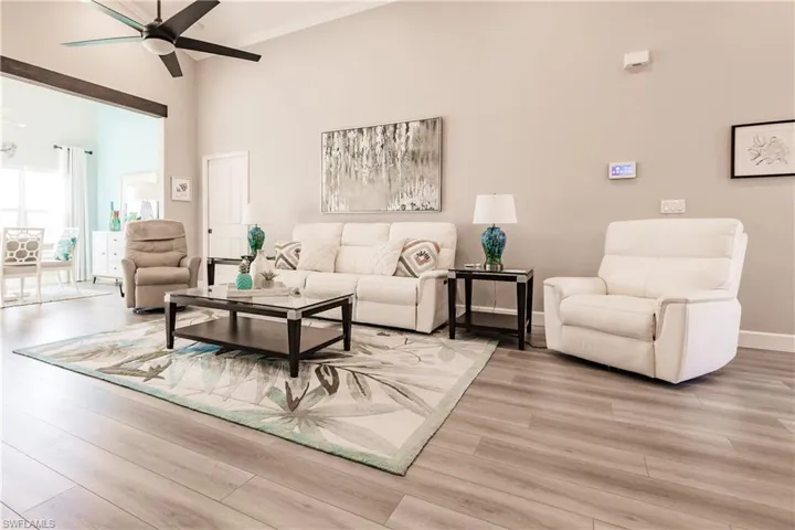 Living room with ceiling fan, a towering ceiling, and light wood-type flooring