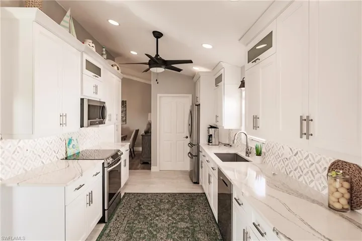 Kitchen featuring light stone counters, sink, white cabinetry, and stainless steel appliances