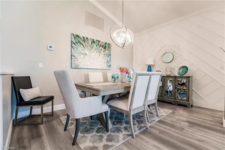 Dining area with lofted ceiling, crown molding, a notable chandelier, and hardwood / wood-style flooring