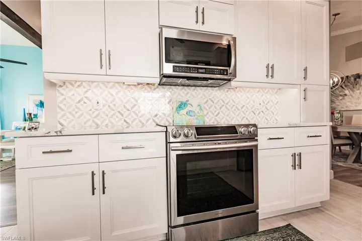 Kitchen featuring tasteful backsplash, light hardwood / wood-style flooring, white cabinets, and appliances with stainless steel finishes
