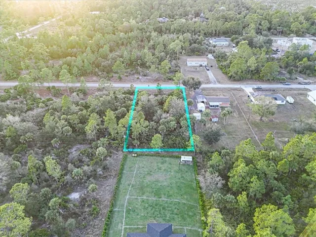 Aerial view of property and surrounding area with property parcel outlined and a heavily wooded area