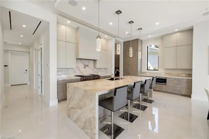 Dual tone kitchen featuring modern cabinets, light stone counters, dual tone cabinetry, an island with sink, and pendant lighting