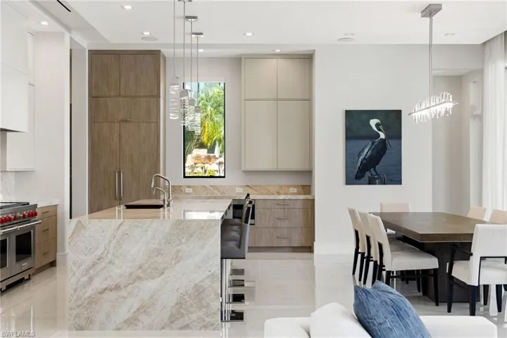 Dual tone kitchen with two tone color scheme, modern cabinets, light stone countertops, range with two ovens, and hanging light fixtures