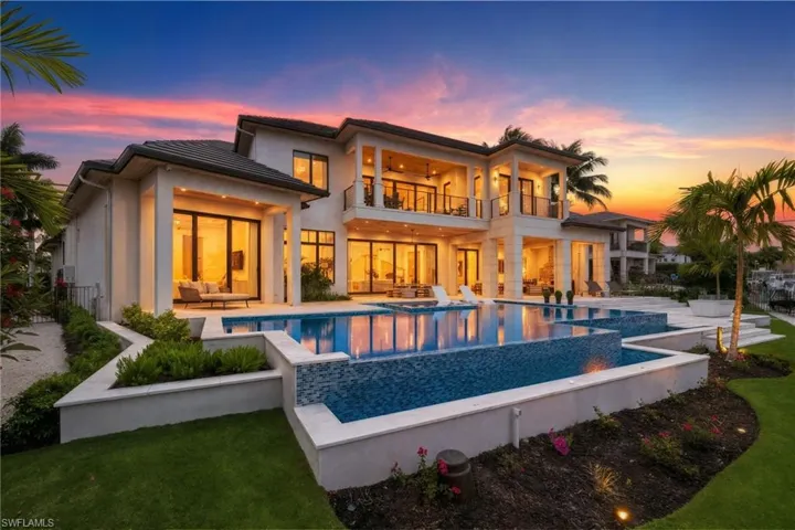 Back of house at dusk featuring a balcony, an infinity pool, a patio area, ceiling fan, and outdoor furniture