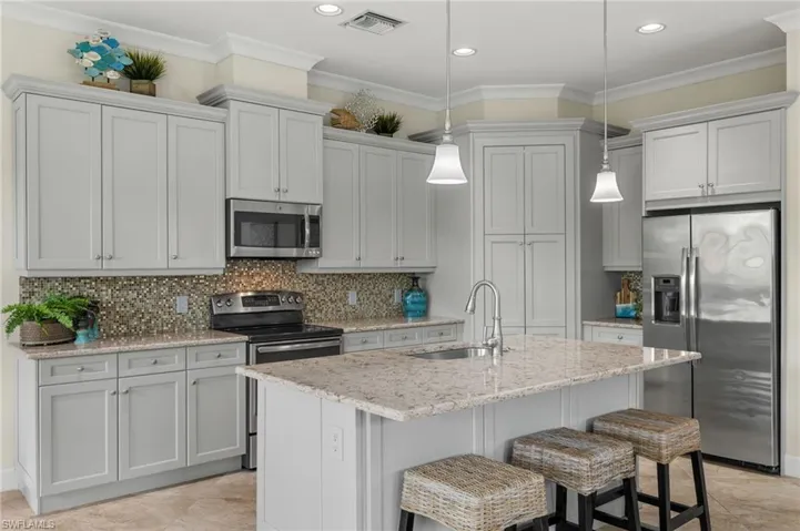 Kitchen with light tile patterned flooring, sink, tasteful backsplash, stainless steel appliances, and a center island with sink