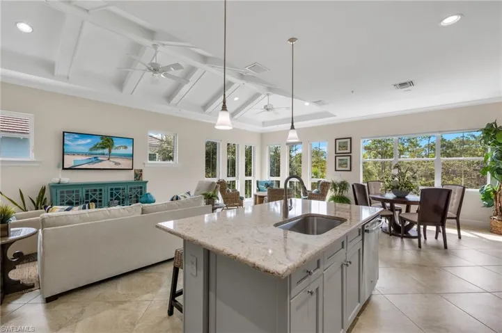 Kitchen featuring light stone countertops, sink, hanging light fixtures, ceiling fan, and a center island with sink