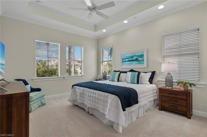 Carpeted bedroom with ceiling fan, a raised ceiling, ornamental molding, and multiple windows