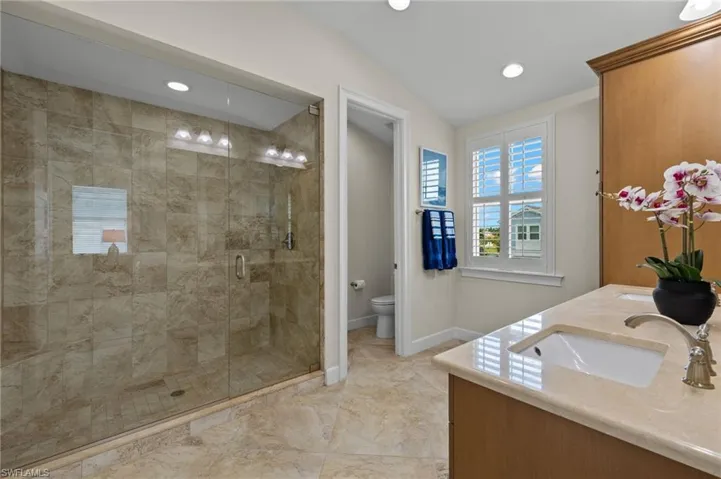Bathroom featuring a shower with door, toilet, double sink vanity, tile patterned floors, and vaulted ceiling