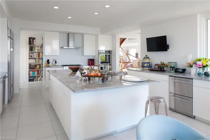 Kitchen with white cabinetry, light stone countertops, wall chimney exhaust hood, light tile patterned floors, and recessed lighting