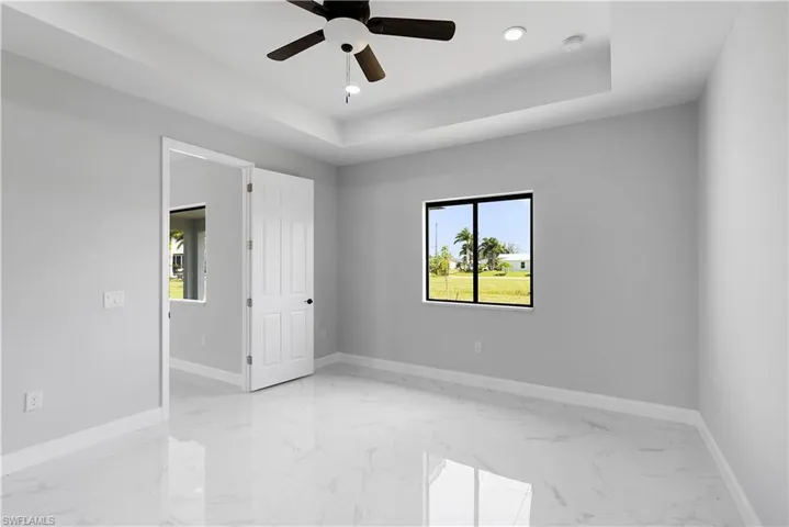 Tiled empty room featuring a tray ceiling and ceiling fan