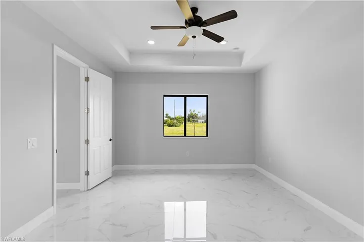 Unfurnished bedroom with ceiling fan, a raised ceiling, and light tile patterned floors