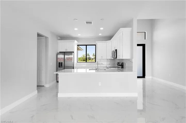 Kitchen with appliances with stainless steel finishes, backsplash, white cabinetry, sink, and light tile patterned flooring