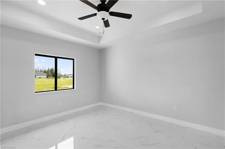 Tiled empty room featuring ceiling fan and a tray ceiling