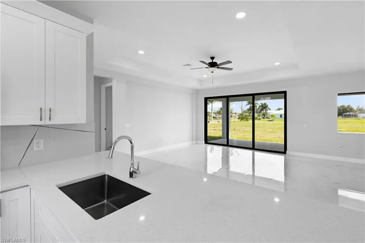 Kitchen with sink, light stone countertops, ceiling fan, a raised ceiling, and white cabinets