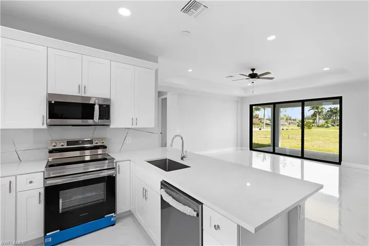 Kitchen with ceiling fan, a tray ceiling, range, dishwasher, and sink
