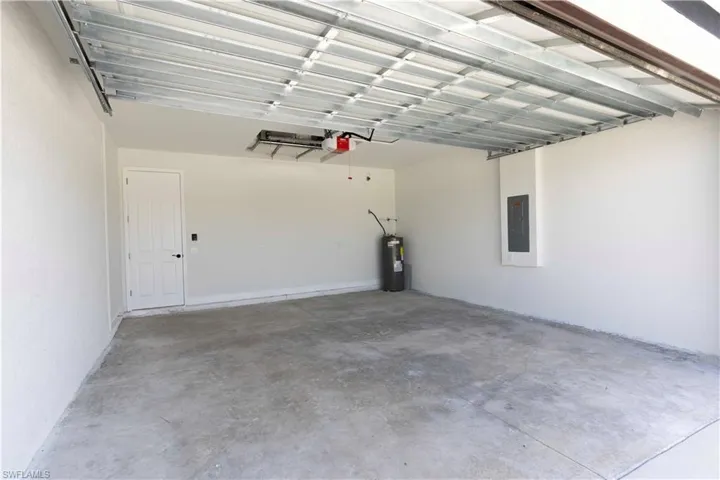 Garage with a garage door opener, electric panel, and electric water heater