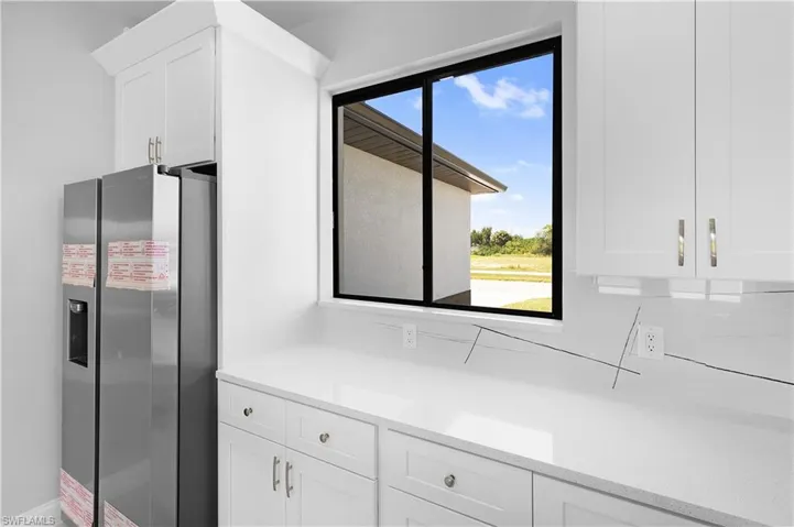 Kitchen with white cabinetry, a wealth of natural light, stainless steel fridge, and light stone countertops