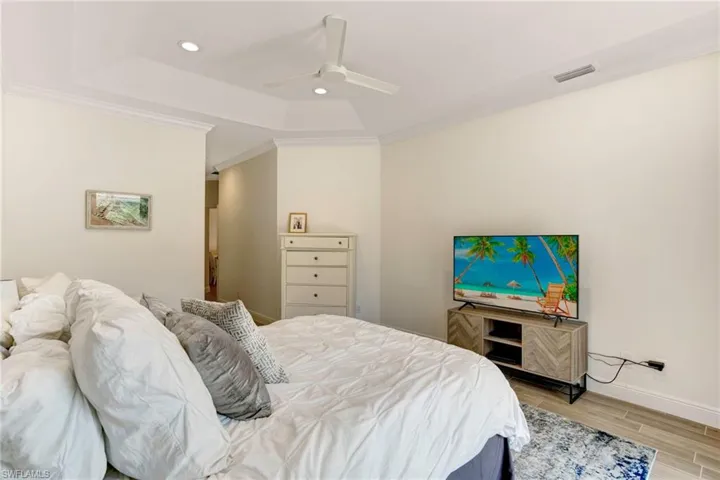 Bedroom with ceiling fan, a tray ceiling, light wood-type flooring, and ornamental molding