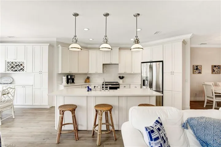Kitchen with light hardwood / wood-style floors, stainless steel fridge with ice dispenser, backsplash, hanging light fixtures, and a kitchen island with sink