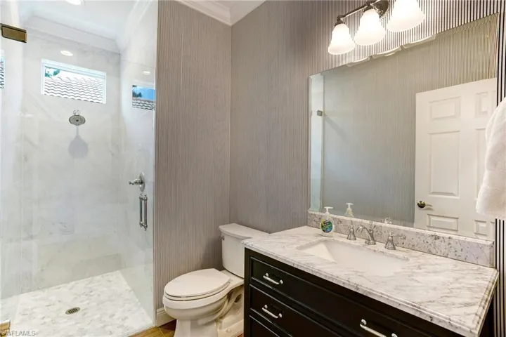 Bathroom with a shower with shower door, vanity with extensive cabinet space, toilet, and crown molding
