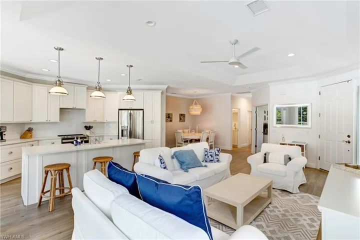 Living room with ceiling fan, sink, a tray ceiling, and light wood-type flooring