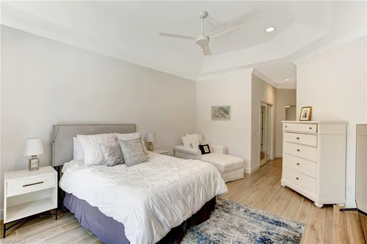 Bedroom with light wood-type flooring, ornamental molding, ceiling fan, and a raised ceiling