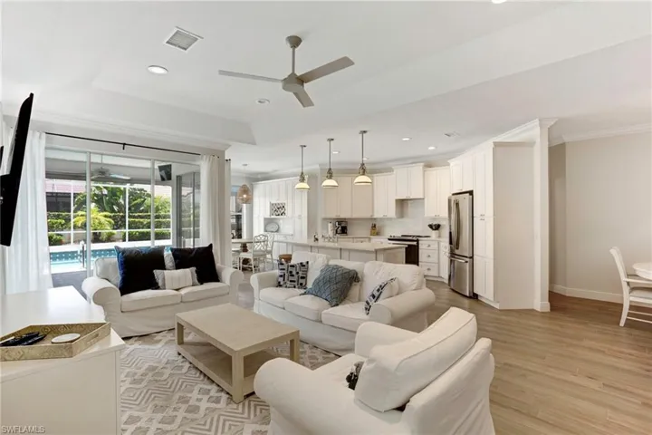 Living room with ceiling fan, a tray ceiling, light wood-type flooring, and crown molding