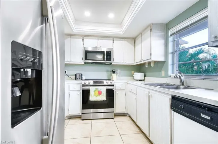 Kitchen with stainless steel appliances, a tray ceiling, light countertops, white cabinetry, and crown molding