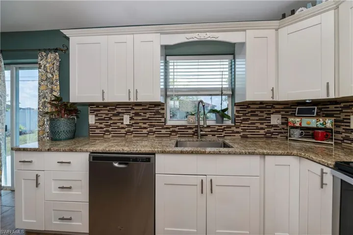 Kitchen featuring a wealth of natural light, dishwasher, white cabinetry, and backsplash