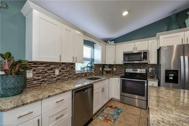 Kitchen with backsplash, stainless steel appliances, white cabinetry, sink, and light tile patterned floors