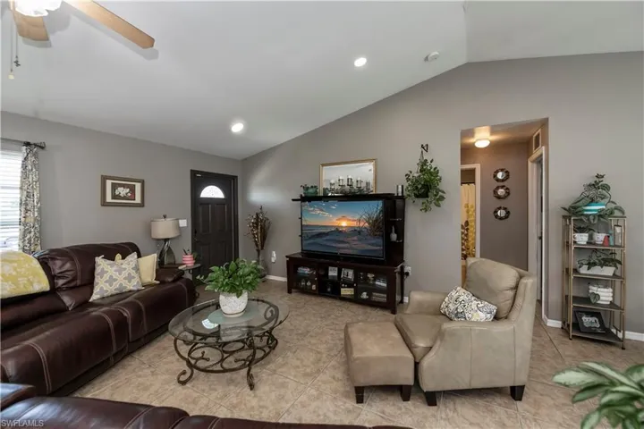 Living room featuring light tile patterned floors, ceiling fan, and lofted ceiling