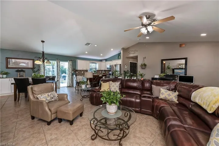 Tiled living room with ceiling fan with notable chandelier and lofted ceiling